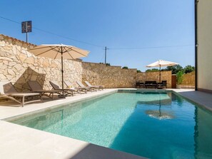 A swimming pool with lounge chairs and umbrellas, surrounded by stone walls and a clear sky. - Villa Miromar Comfortable Holiday Residence (Marcana)