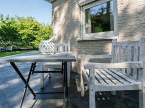 Eine Terrasse mit Tisch und zwei weißen Stühlen, einem dekorativen Laternen und einem Gebäude aus Stein mit einem Fenster.