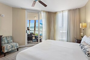 A hotel room with a large bed, a chair, a desk, a lamp, and a view of the outside. - Palms Resort #2203 Jr 2BR (Destin)