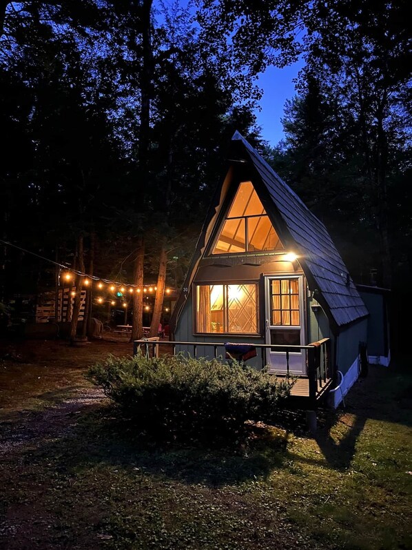 A cabin with a triangular roof, large windows, and a porch area. - Highland Haus - Cozy 70s Aframe - Lake Access (Stoddard)