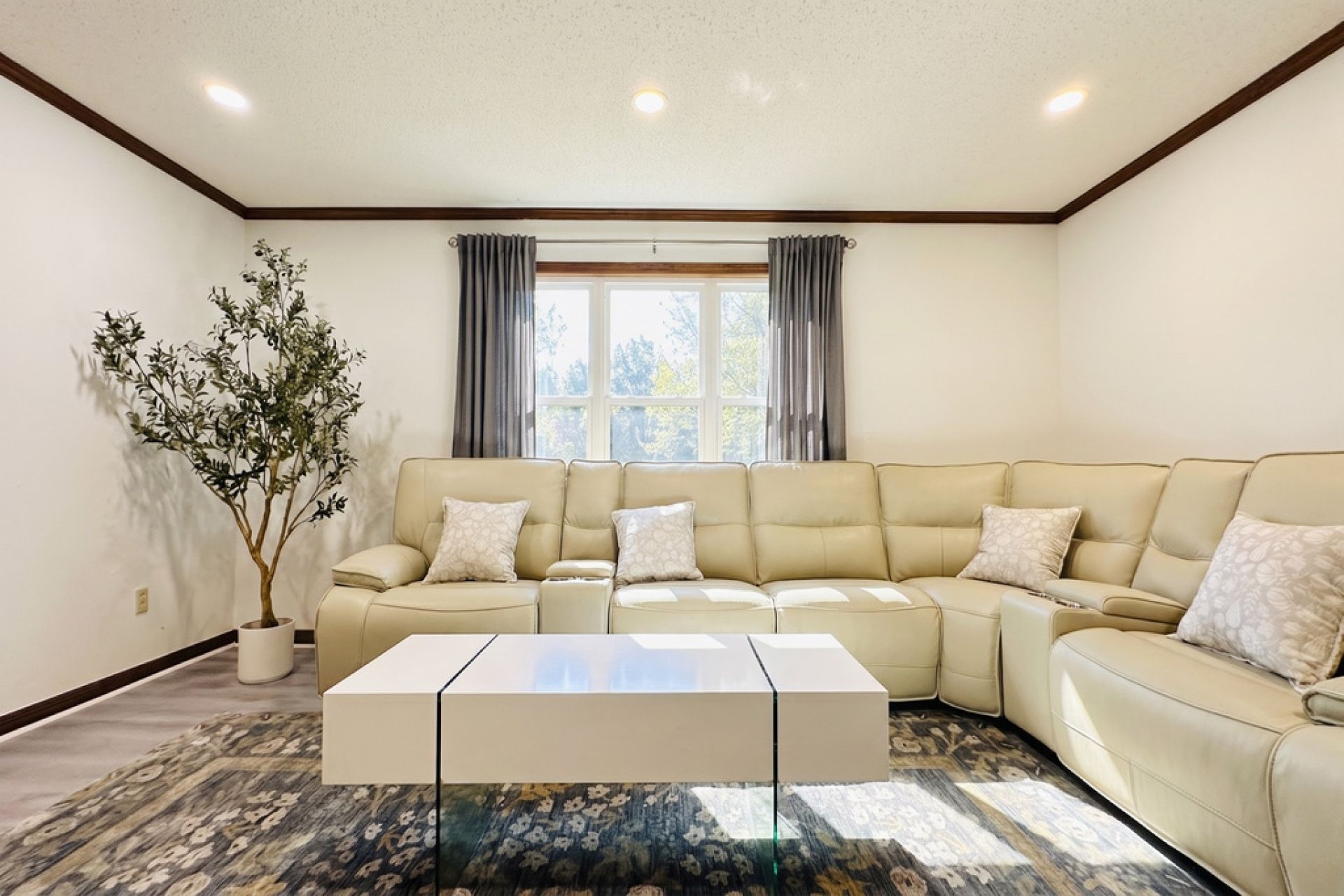 A living room with a beige sectional sofa, a glass coffee table, and a potted plant.