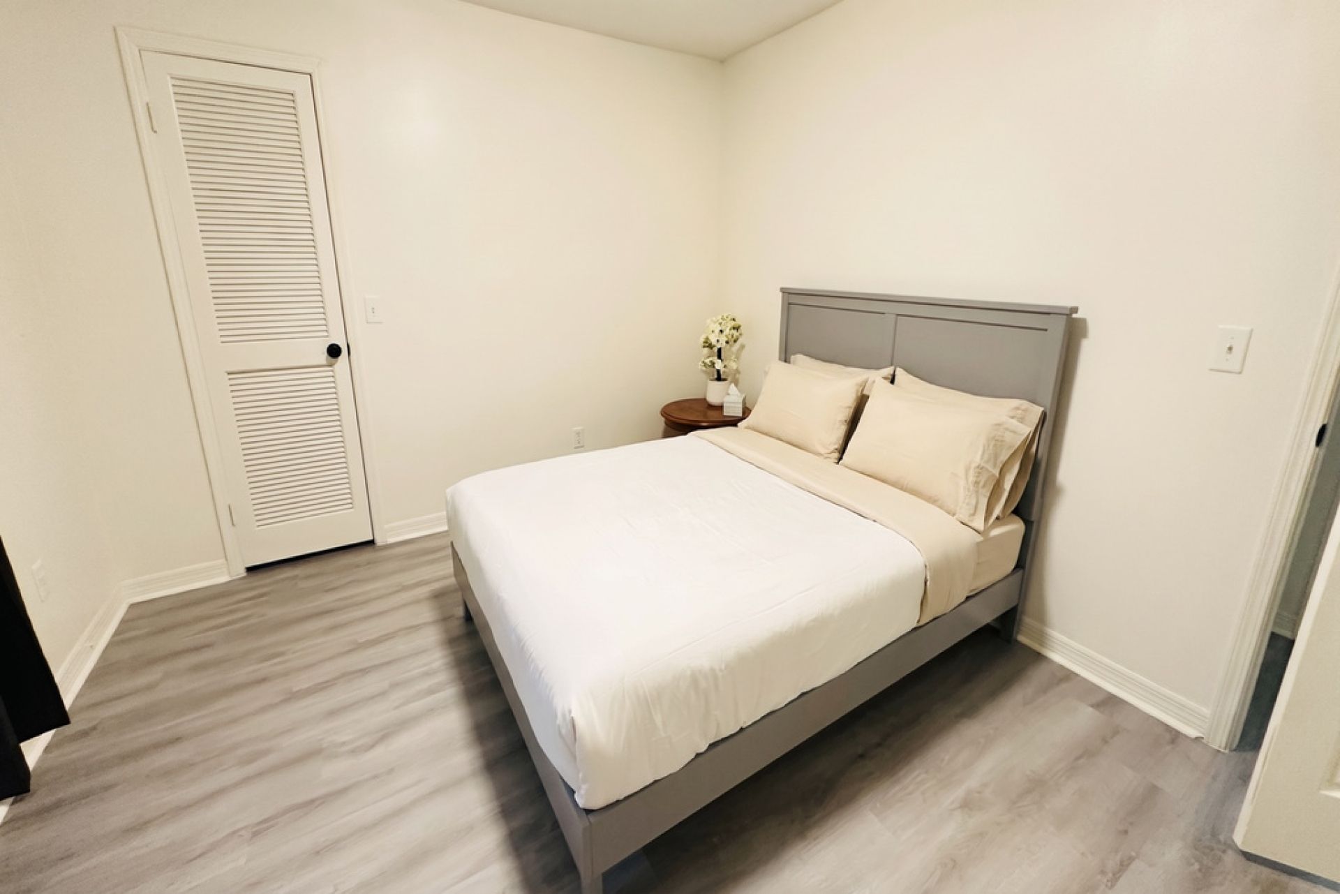 A bedroom with a bed, a nightstand, a wall-mounted shelf, and a door.