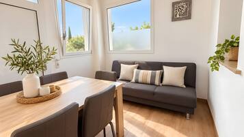 A modern living room with a dining area, large windows, a sofa, and a potted plant.