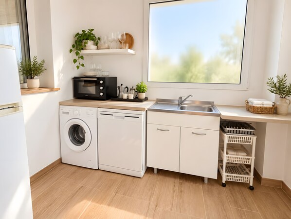 Cocina compacta con lavadora, lavavajillas, microondas y un amplio ventanal.