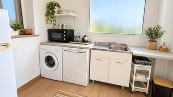 A compact kitchen with a washing machine, a microwave, a sink, and a window with a view.