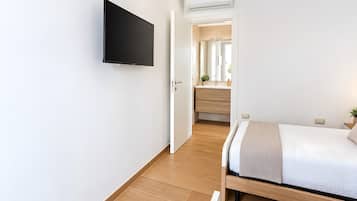 Ein modernes Schlafzimmer mit einem flachbildfernseher an der Wand, einem hölzernen Bett mit weißer Matratze und Holzboden.