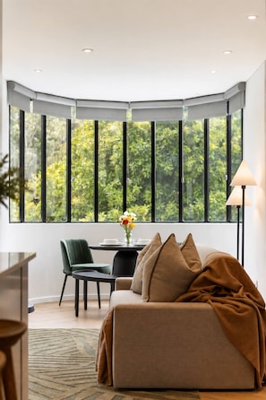 Une pièce moderne avec une fenêtre d’angle incurvée, un canapé, un fauteuil, une table avec un vase et un lampadaire.