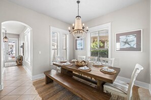 A dining room with a wooden table set for four, white chairs, a chandelier, and a framed picture on the wall. - Sunshine Shack (Panama City Beach)