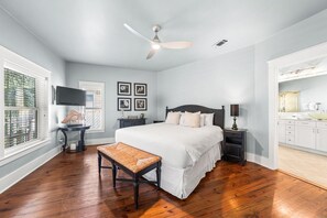 A bedroom with a bed, bedside tables, a bench, a ceiling fan, a TV, and a window with blinds. - Sunshine Shack (Panama City Beach)
