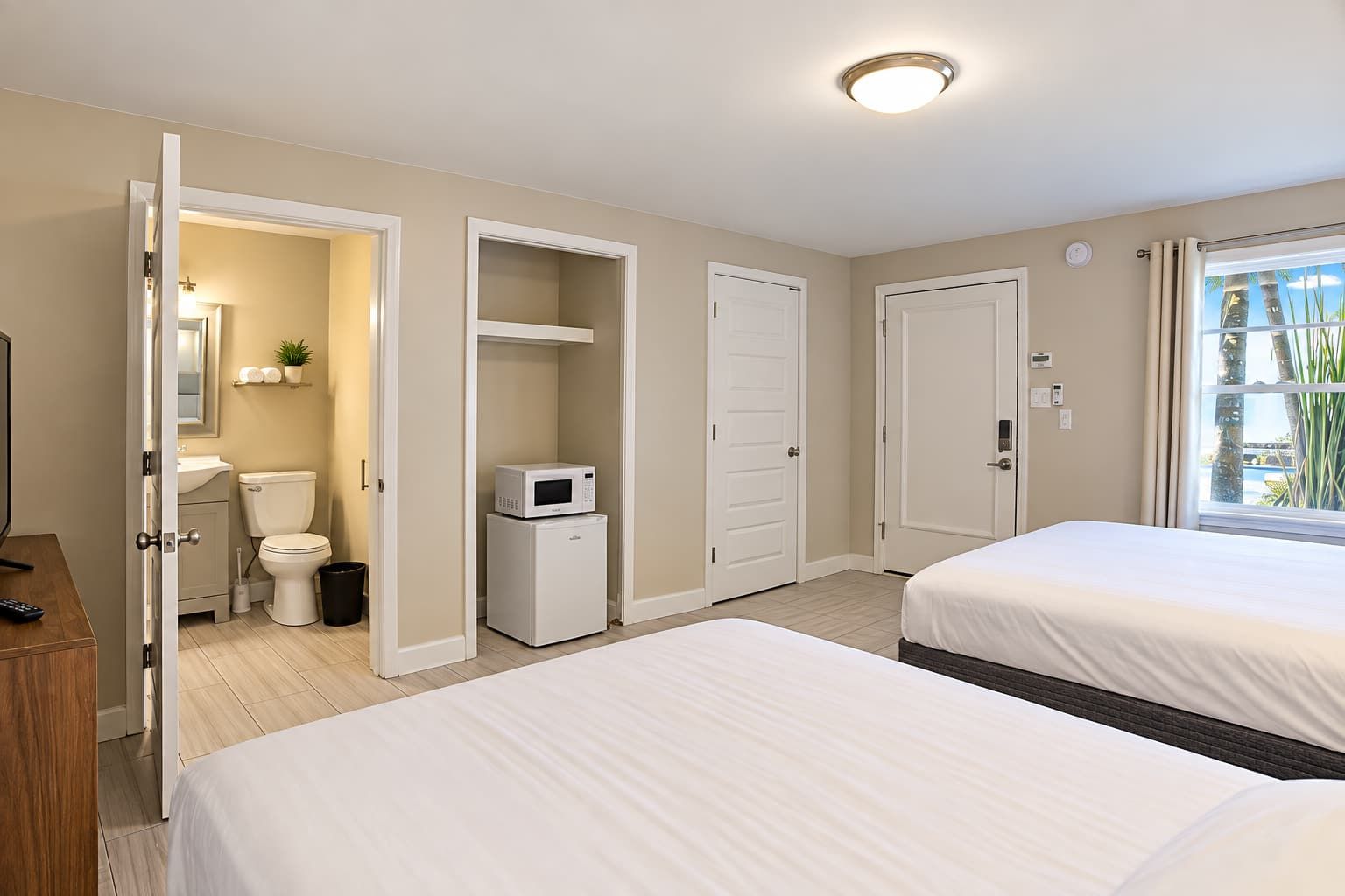 Een hotelkamer met twee bedden, een badkamer en uitzicht op palmbomen.