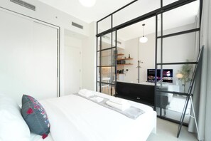 Ein modernes Hotelzimmer mit Bett, großem Spiegel, Fernseher und einer Küchenzeile.