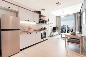 Une cuisine moderne équipée d’un réfrigérateur, d’un four et d’un four à micro-ondes intégrés. On y trouve un coin repas avec une table et des chaises, ainsi qu’une vue sur la ville grâce à de grandes fenêtres.
