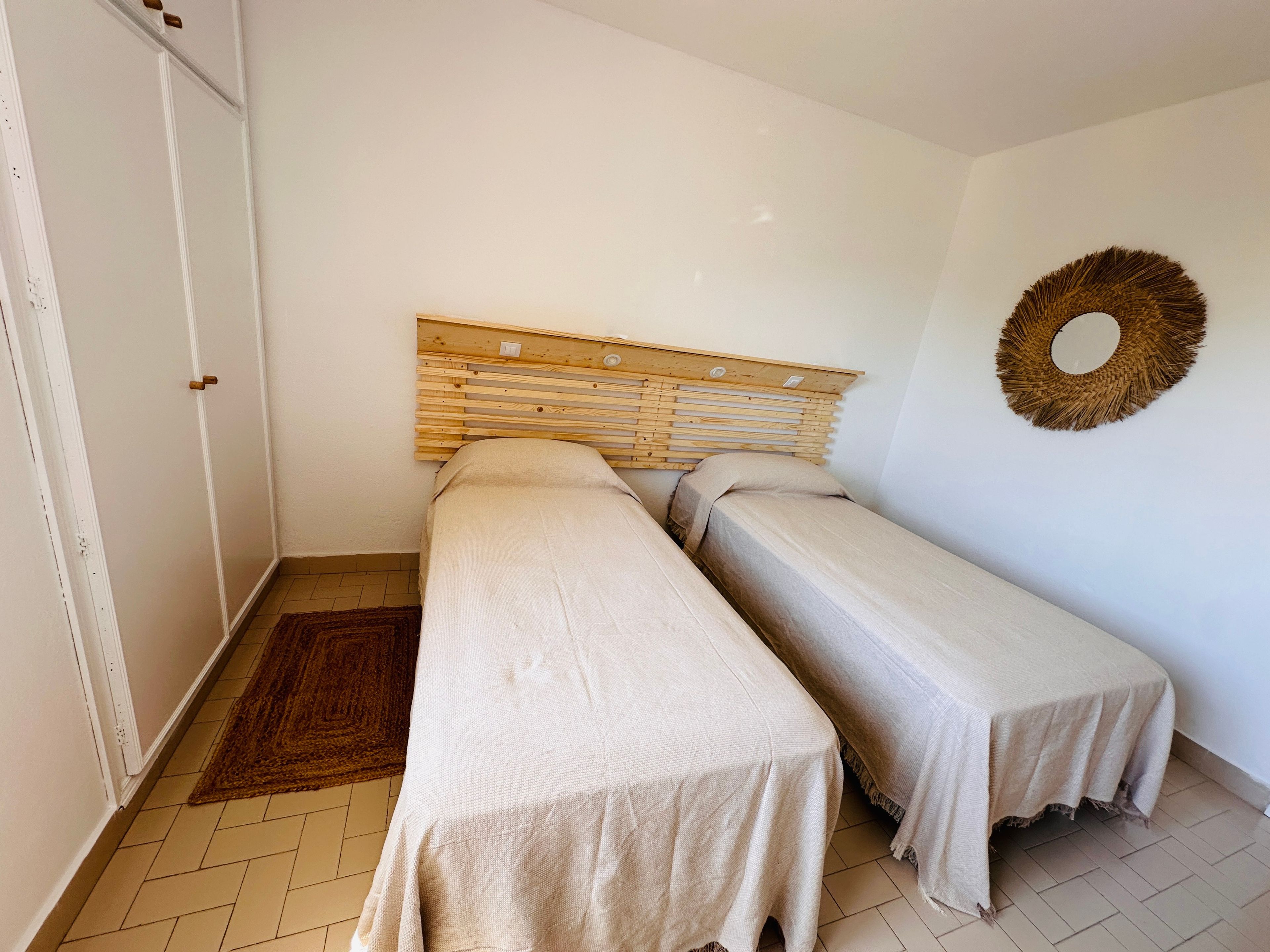 Een kamer met twee eenpersoonsbedden, een houten hoofdbord, een wanddecoratie van geweven materiaal en een betegelde vloer.