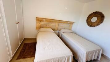 Een kamer met twee eenpersoonsbedden, een houten hoofdbord, een wanddecoratie van geweven materiaal en een betegelde vloer.