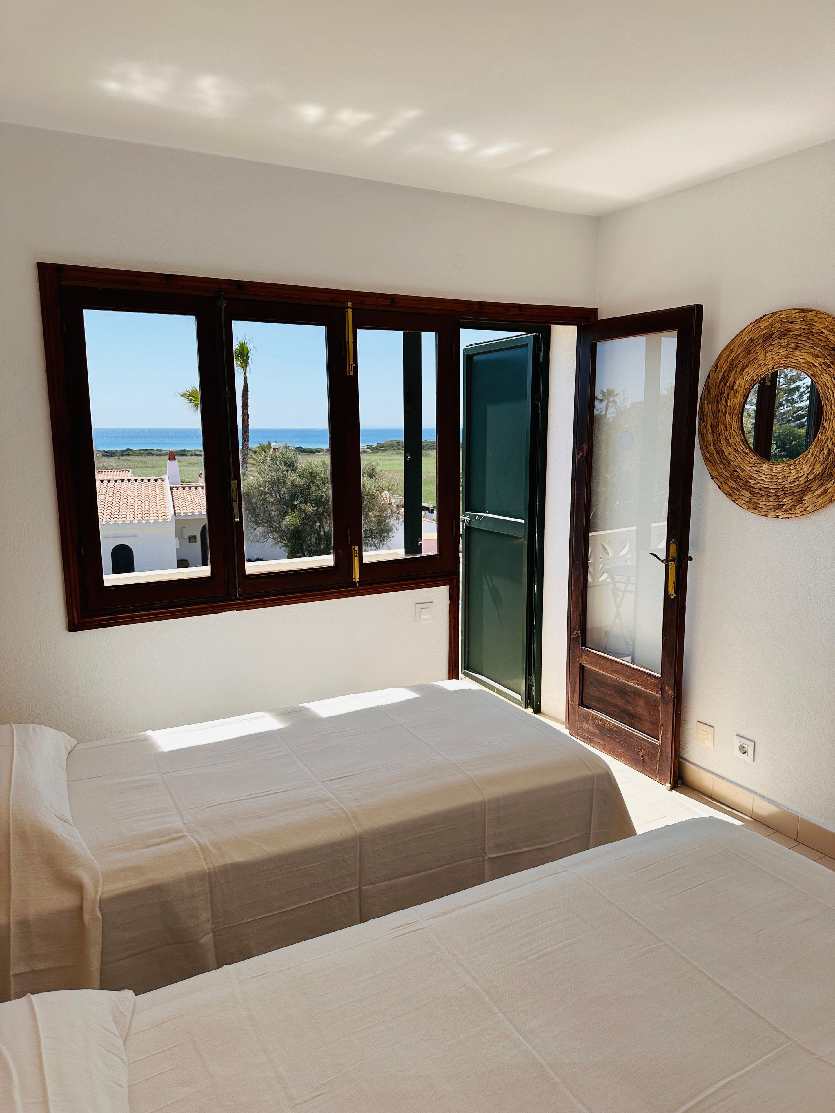 A bedroom with a bed, a window with a view of the sea, and a woven wall decoration.