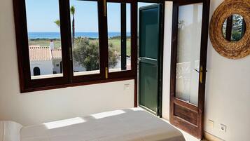 A bedroom with a bed, a window with a view of the sea, and a woven wall decoration.