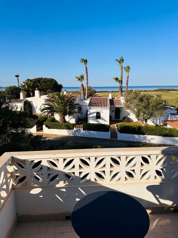 A terrace with a view of a coastal landscape, including palm trees and a clear sky.
