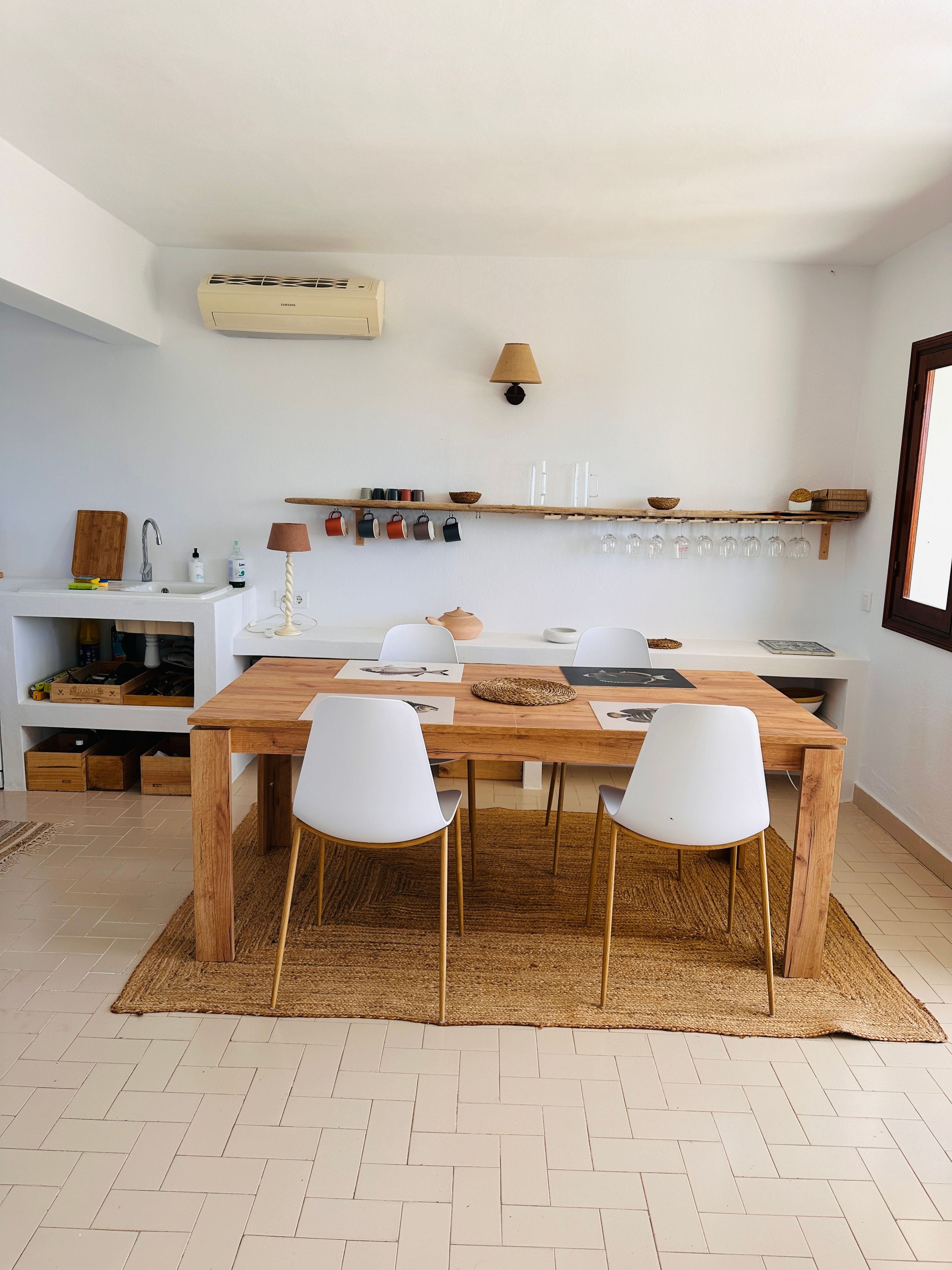 Een moderne keuken met een houten tafel, witte stoelen en een hangplank met keukengerei.