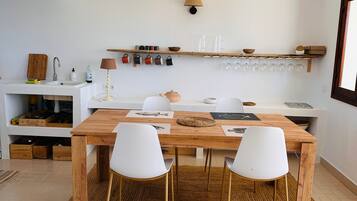 Een moderne keuken met een houten tafel, witte stoelen en een hangplank met keukengerei.