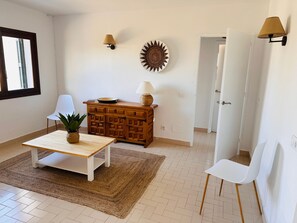A room with a wooden cabinet, a white table with a plant, two white chairs, a woven rug, and a wall-mounted lamp. - Villa 'Sa Pitxuri' with pool, sea view, Wi-Fi and air conditioning (Torresolí)