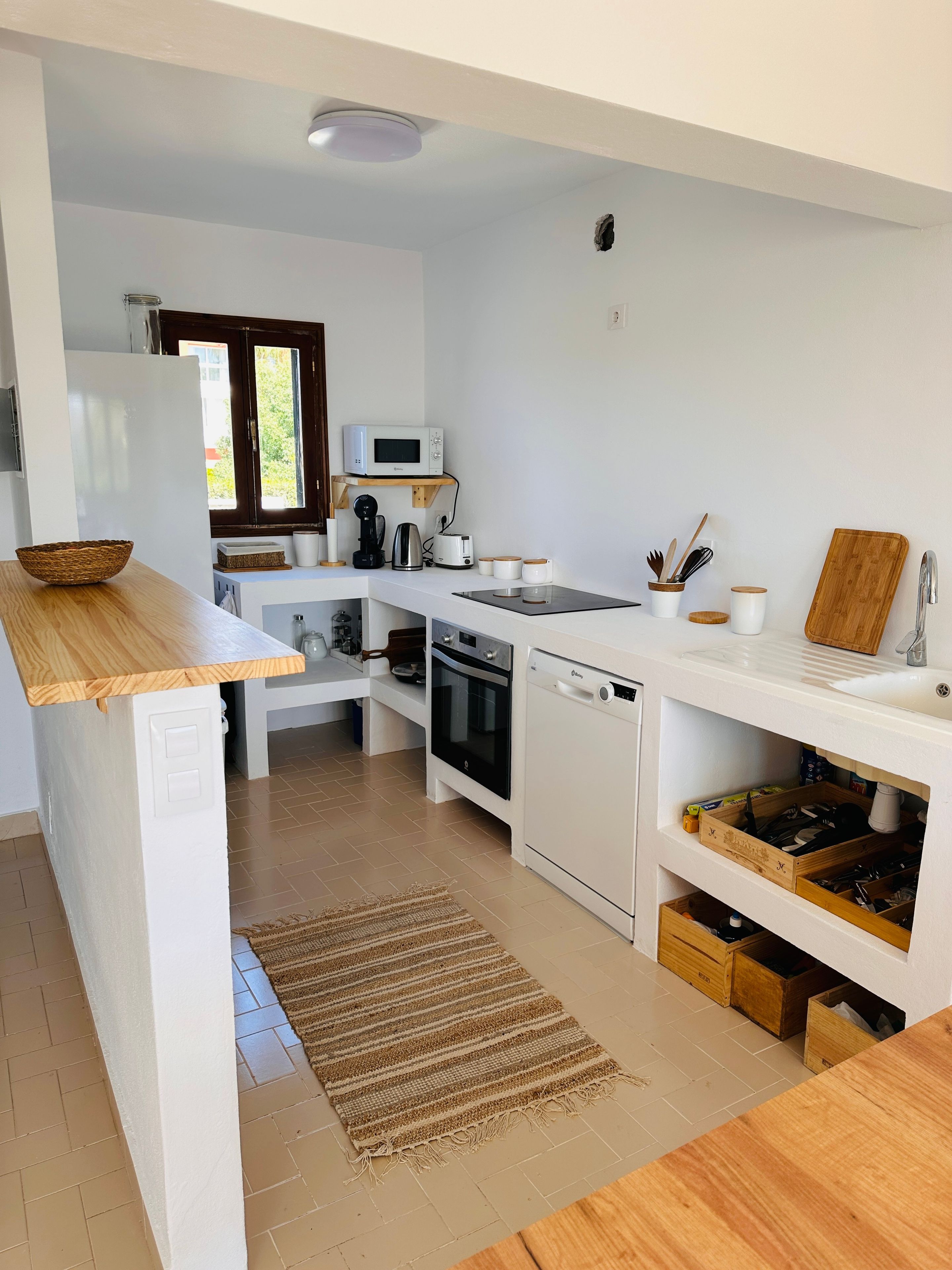 Une cuisine moderne avec des meubles blancs, un four à micro-ondes, une machine à café et des plans de travail en bois.