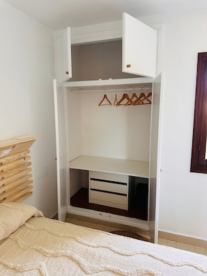 Un vestidor amplio con perchas de madera, una cama con una colcha color beige y un estante de madera.