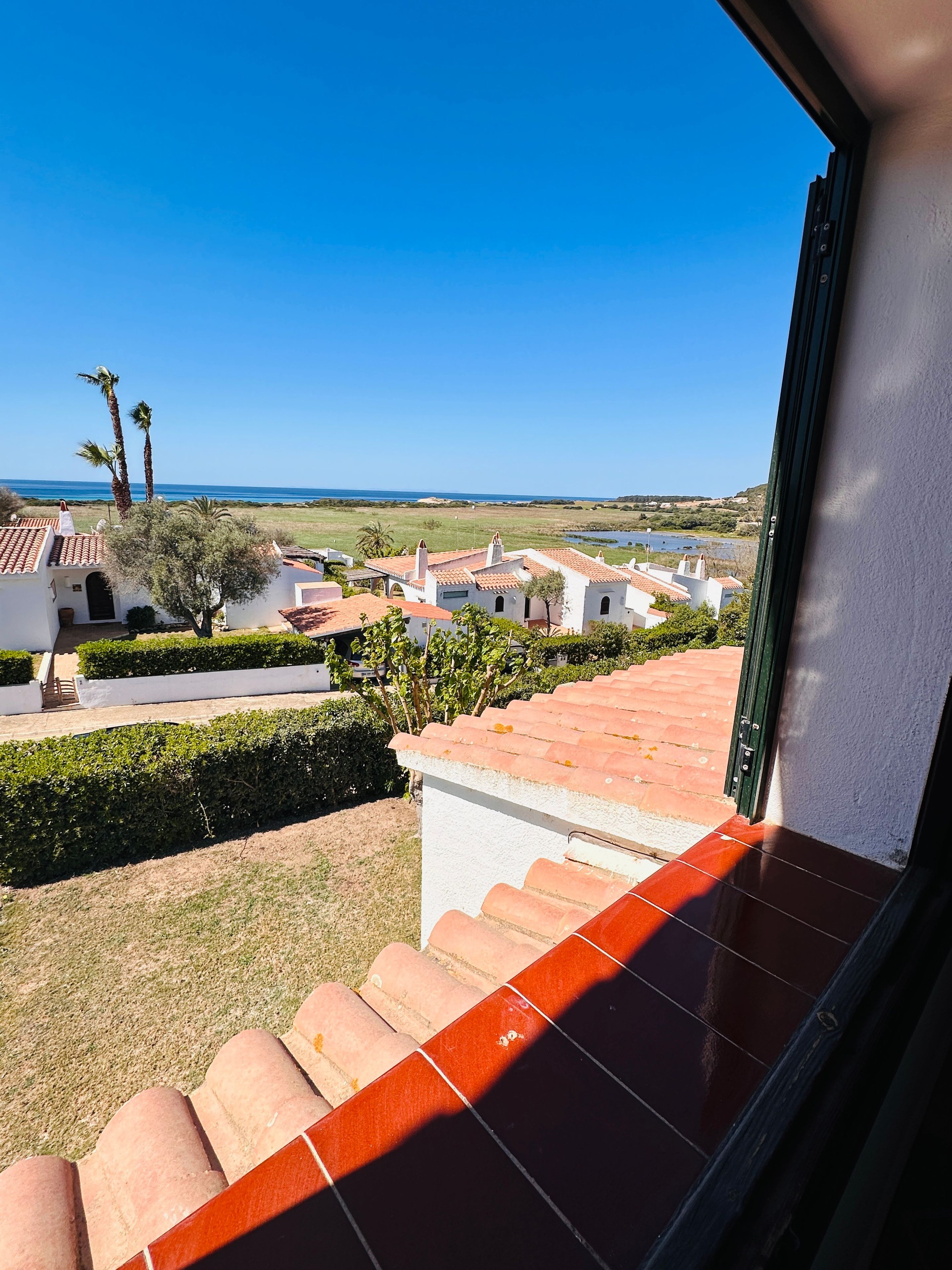 A view from a window overlooking a coastal area with buildings, a clear sky, and a body of water.