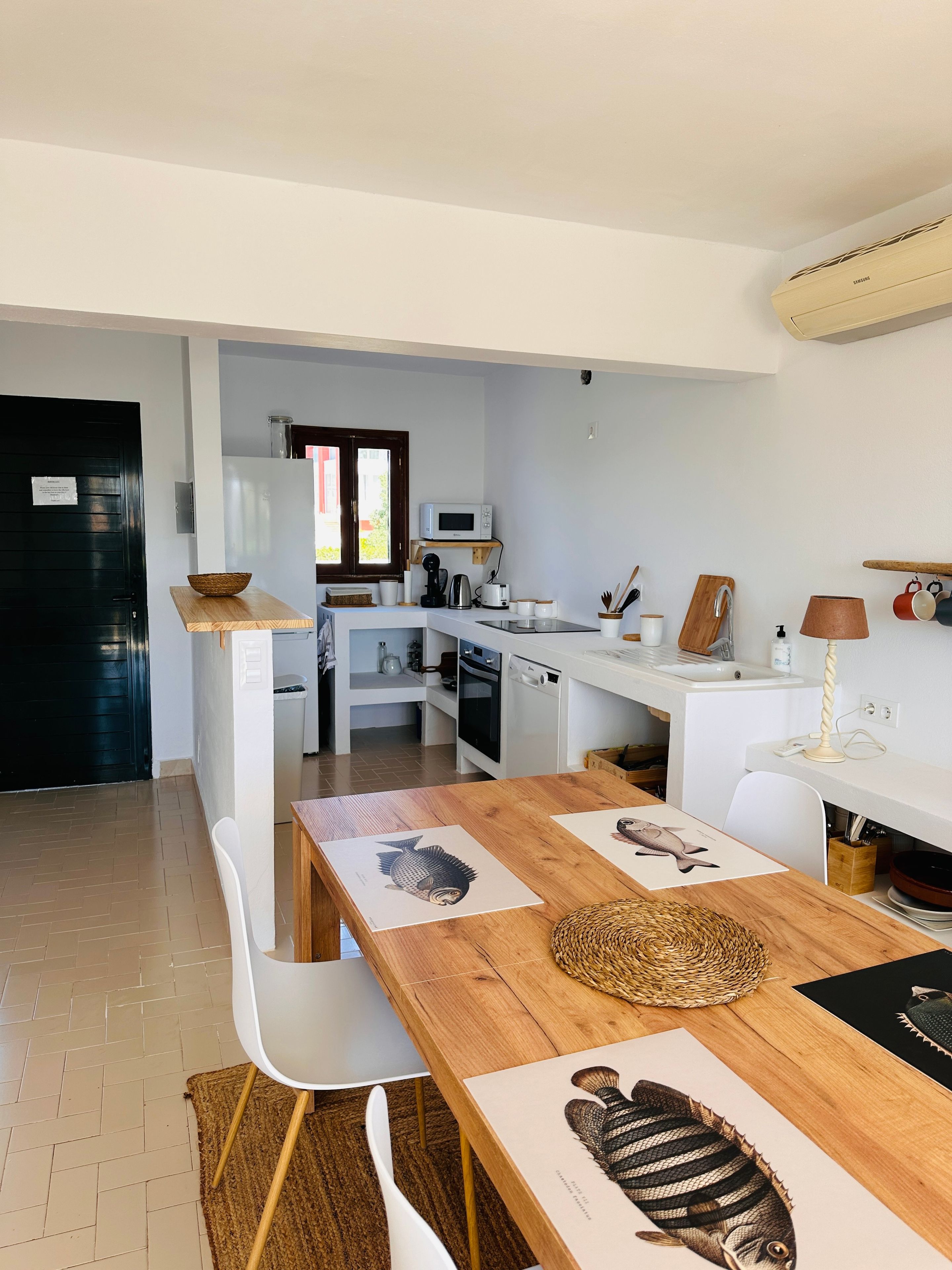 A modern kitchen with white appliances, a dining table with artwork, and a black door.