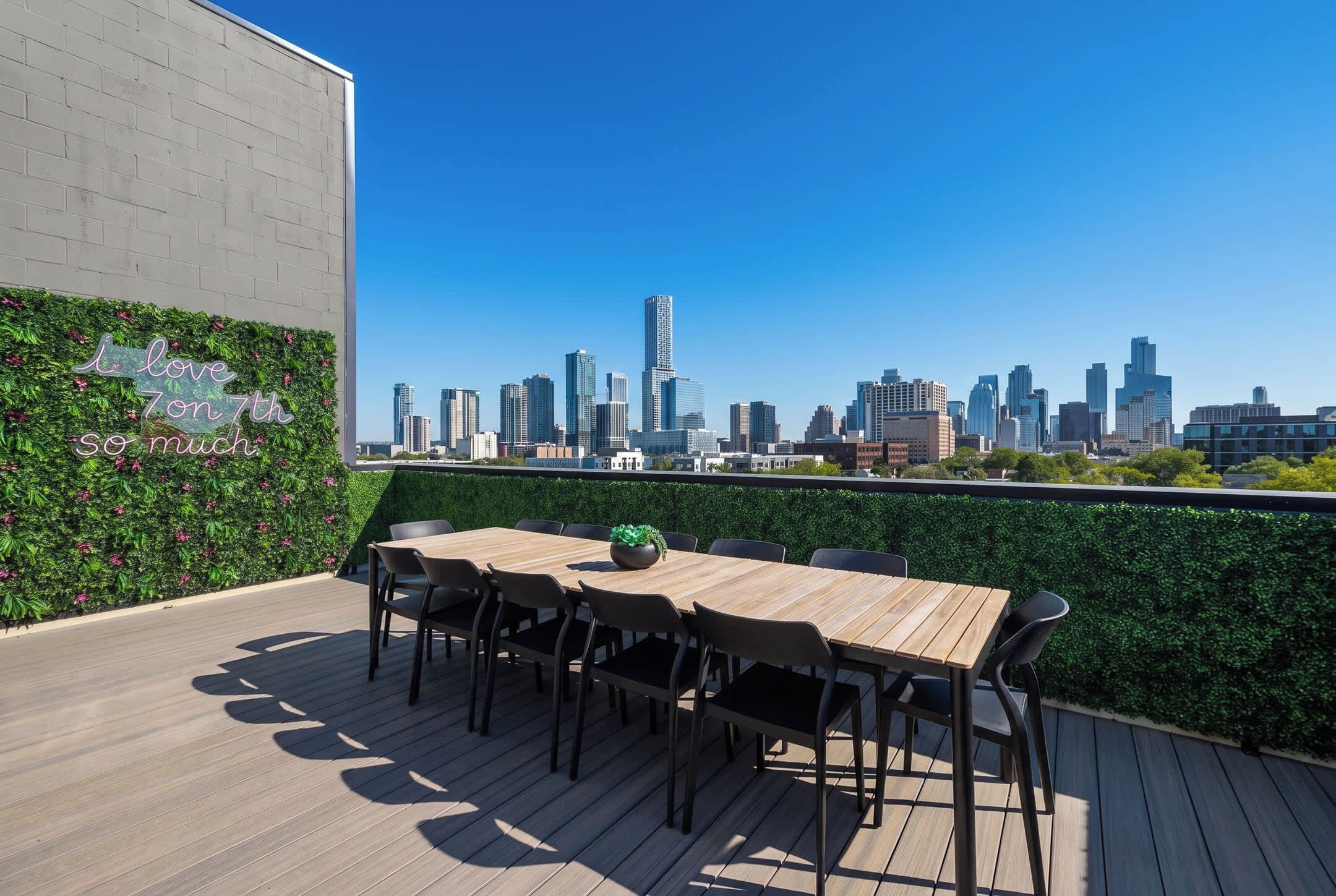 Eine Dachterrasse mit Blick auf die Stadtlandschaft, einem Holztisch mit Stühlen und einer Wand mit Pflanzenzierde.