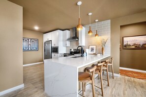 A modern kitchen with a marble island, stainless steel appliances, pendant lighting, and a bar area with wooden stools. - Walkable 2BR Suite + Rooftop Retreat | East Austin (Austin)