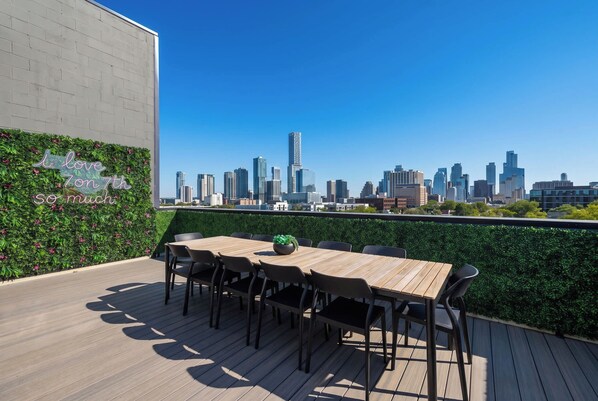 A rooftop terrace with a city skyline view, a wooden table with chairs, and a decorative wall with greenery. - Walkable 2BR Suite + Rooftop Retreat | East Austin (Austin)