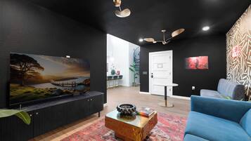 Ein modernes Wohnzimmer mit einem großen Flachbildfernseher, einem blauen Sofa, einem Couchtisch und einem gemusterten Teppich.