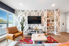 A modern living room with a leather armchair, a coffee table, a TV mounted on the wall, and a cactus plant. - 3 Suites, Full 4th Floor Rental + Rooftop Retreat (Austin)
