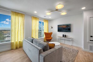 Ein modernes Wohnzimmer mit einem grauen Sofa, einem orangefarbenen Sessel, einem kleinen runden Tisch und einem Gemälde an der Wand.