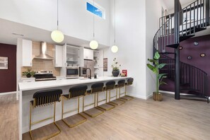 A modern kitchen with white cabinets, a central island with bar stools, and a spiral staircase. - 3 Suites, Full 4th Floor Rental + Rooftop Retreat (Austin)