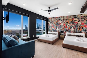 A modern bedroom with two beds, a blue sofa, and a city view. - 3 Suites, Full 4th Floor Rental + Rooftop Retreat (Austin)