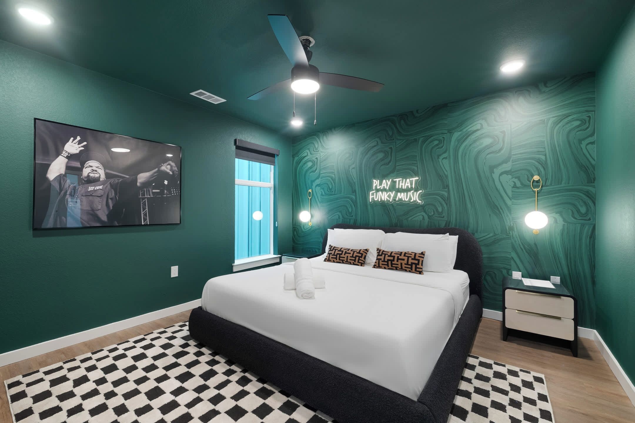 Ein modernes Schlafzimmer mit einem Bett, einem Deckenventilator, einem an der Wand montierten Fernseher und einem Neon-Leuchtschild.