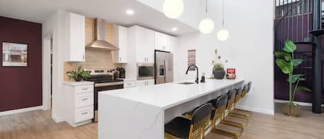 A modern kitchen with white cabinetry, a marble island, and a bar area with gold chairs.