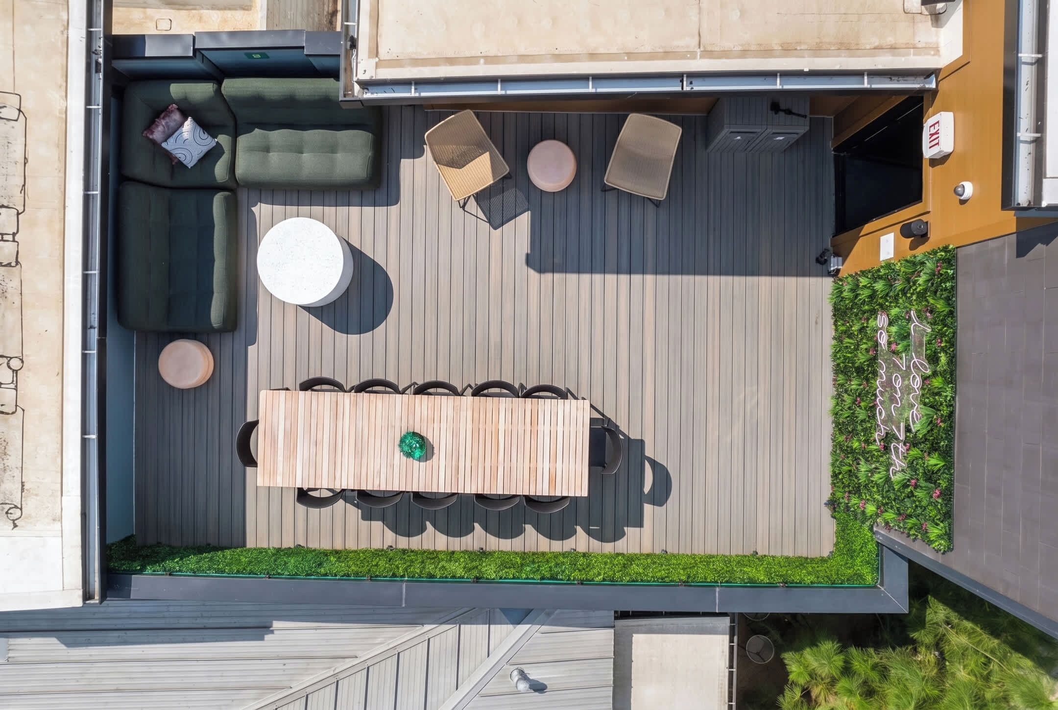 Eine Terrasse im Freien mit einem Holztisch und Stühlen, einem runden weißen Tisch und einer gepolsterten grünen Sitzgruppe.