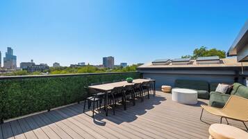 A rooftop terrace with a city skyline view, a table with chairs, and a sofa.