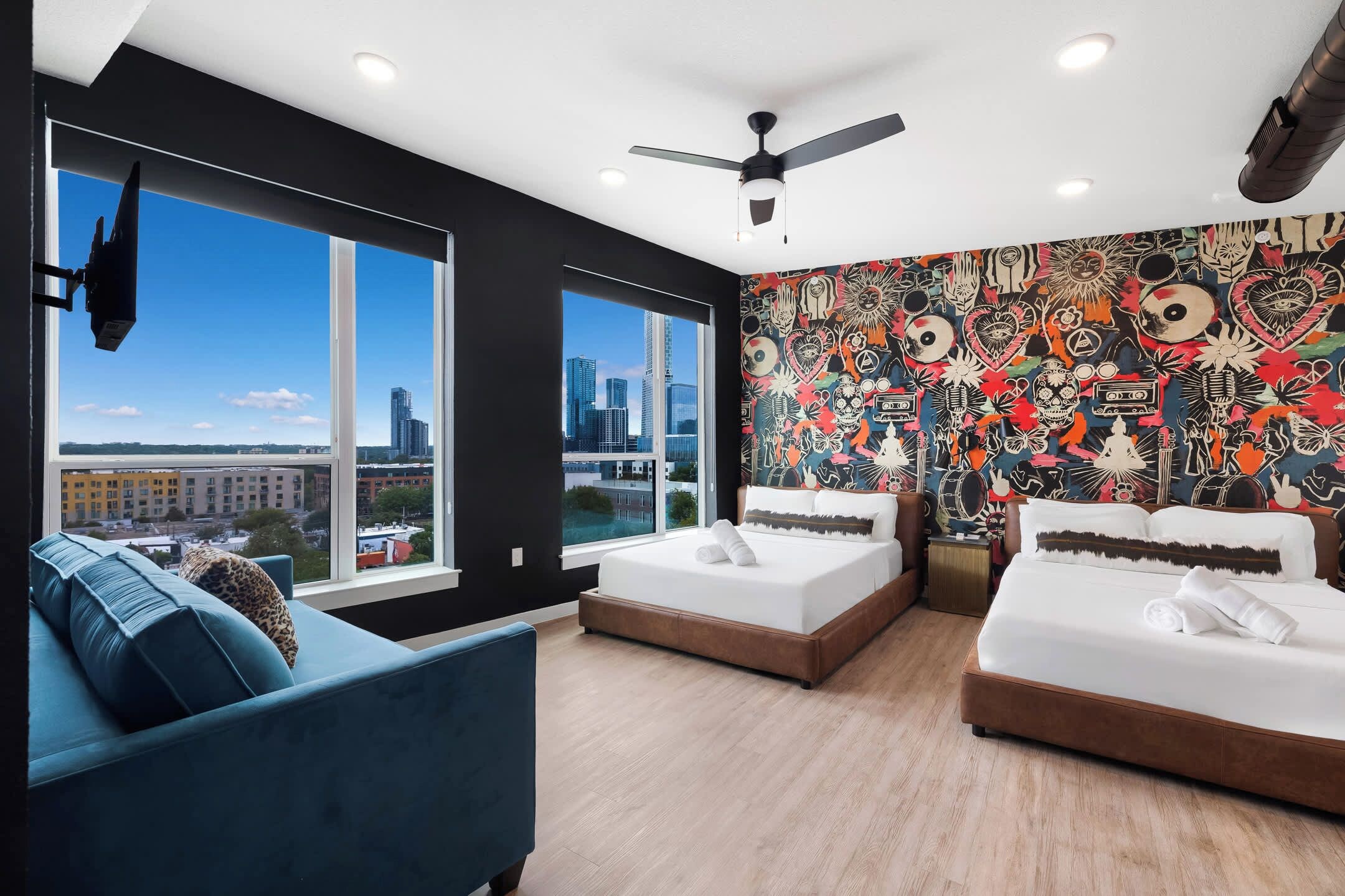 Ein modernes Schlafzimmer mit zwei Betten, einem blauen Sofa und Blick auf die Stadt.