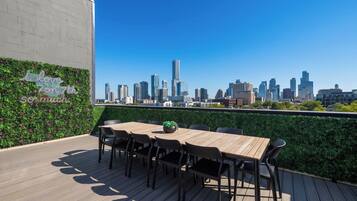 Eine Dachterrasse mit Blick auf die Stadtlandschaft, einem Holztisch mit Stühlen und einer Wand mit Pflanzenzierde.