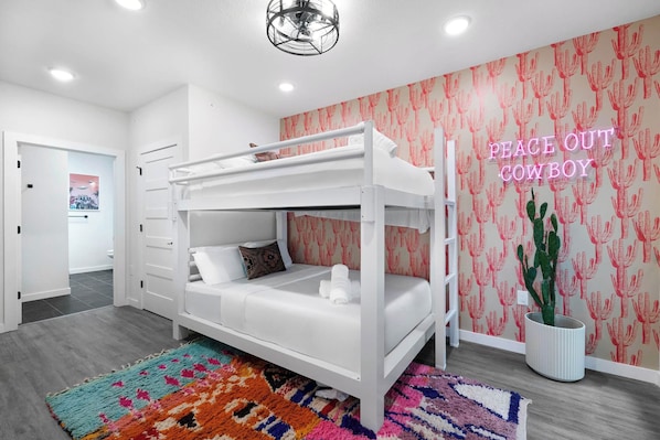 Dormitorio con literas, un letrero de neón, una planta de cactus y una alfombra colorida.