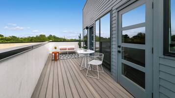 Eine Holzterrasse mit Tisch und Stühlen, eine kleine Sitzecke und eine Glastür, die sich öffnen lässt.