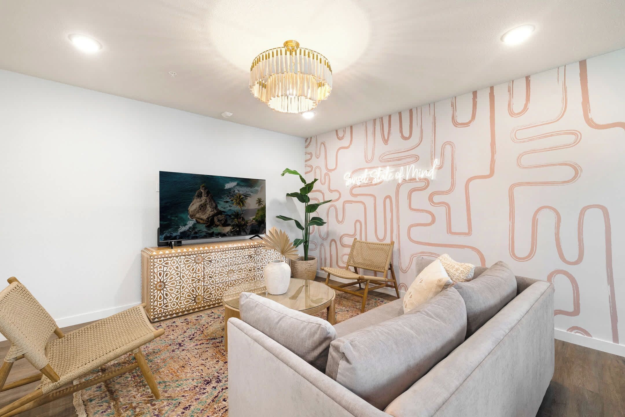 Ein modernes Wohnzimmer mit Sofa, Sesseln, Fernseher, einer Wanddekoration und einem Chandelier.
