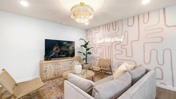 Ein modernes Wohnzimmer mit Sofa, Sesseln, Fernseher, einer Wanddekoration und einem Chandelier.