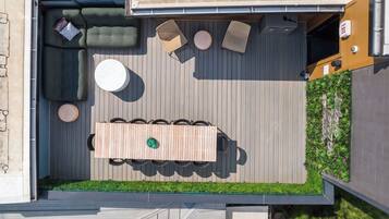 Eine Terrasse im Freien mit einem Holztisch und Stühlen, einem runden weißen Tisch und einer gepolsterten grünen Sitzgruppe.