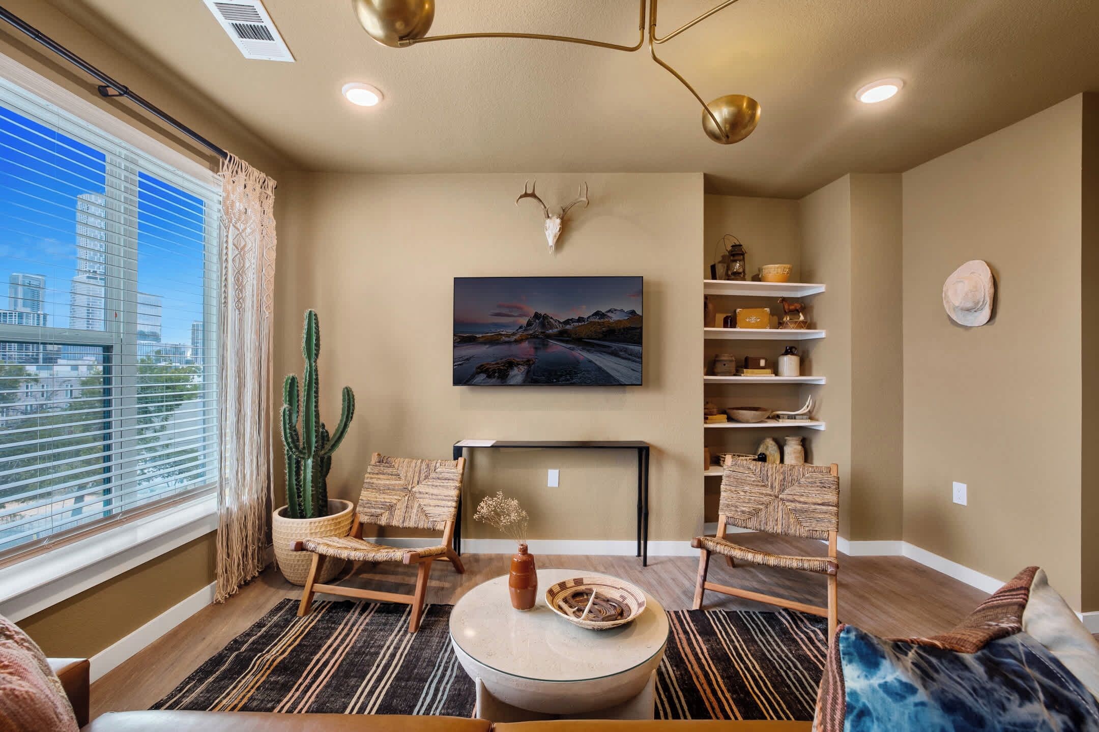 A modern living room with a large window, a cactus, a fireplace, and a city view.