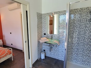 Ein Badezimmer mit einem Glaswaschbecken, einem Spiegel und einer Duschkabine mit Fliesenwand.