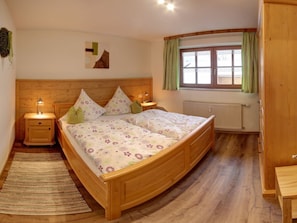 A bedroom with a wooden bed, bedside lamps, a radiator, and a window with curtains. - No. 4 Frillensee "beim Bretzner" (Inzell)